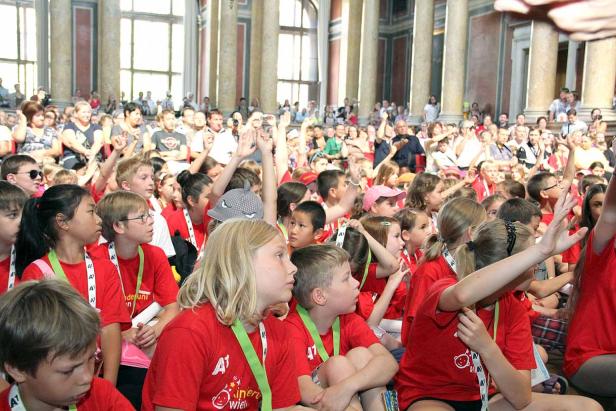Eine große Gruppe Kinder und Erwachsene in einem großen Raum mit Säulen.