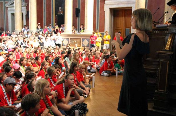 Eine Frau hält vor einer Gruppe von Kindern in roten T-Shirts eine Rede.