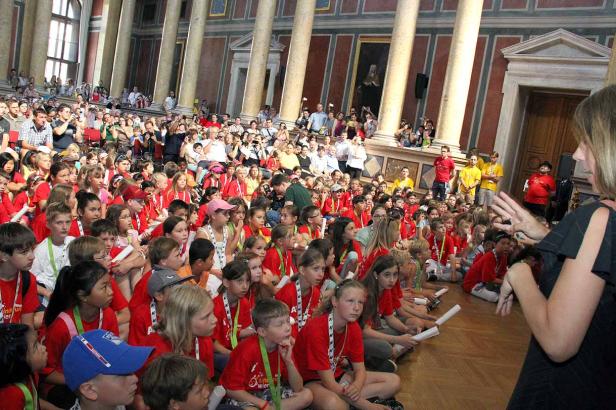Eine große Gruppe von Kindern sitzt auf dem Boden in einem großen Saal.