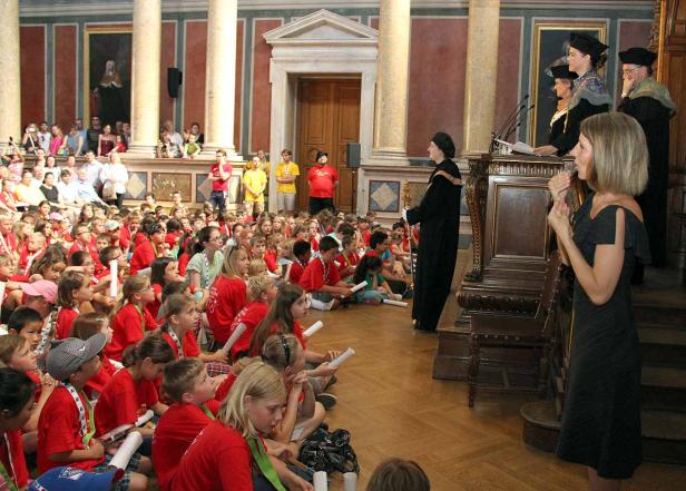 Eine Gruppe Kinder sitzt auf dem Boden und hört einer Rede zu.