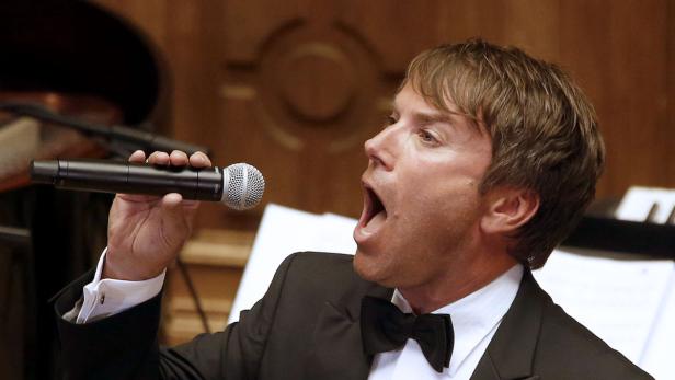 Ein Mann im Anzug singt mit offenem Mund in ein Mikrofon.