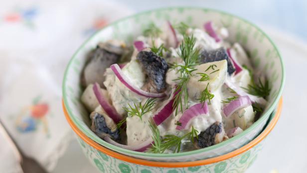 Ein Schüssel mit Heringssalat, garniert mit Dill und roten Zwiebeln.