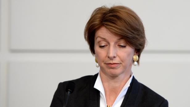 Eine Frau mit braunen Haaren und Ohrringen blickt nach unten.