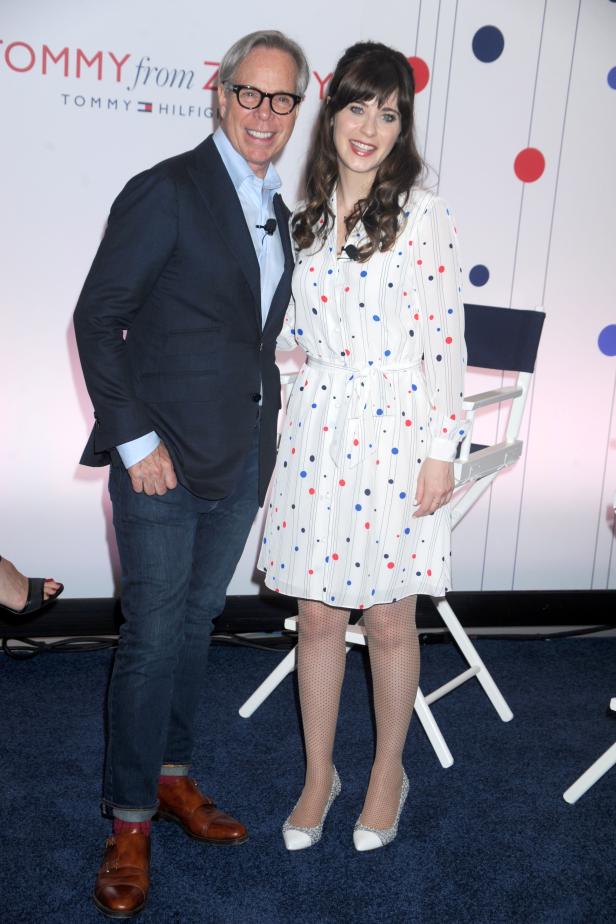 Tommy Hilfiger und Zooey Deschanel posieren zusammen vor einer Wand mit dem Tommy-Hilfiger-Logo.