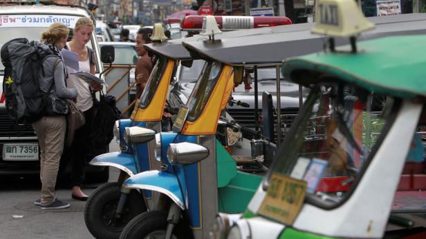 Zwei Touristinnen mit Rucksäcken suchen auf der Straße nach dem Weg, im Hintergrund Tuk-Tuks.