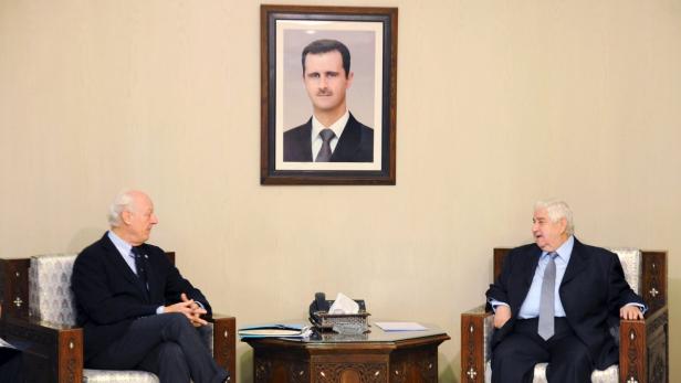 Zwei Männer sitzen sich gegenüber unter einem Porträt von Baschar al-Assad.