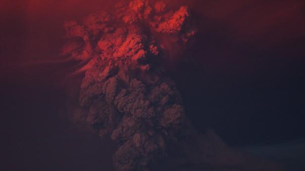 Ein Vulkanausbruch schleudert eine rote Rauchwolke in den Himmel.
