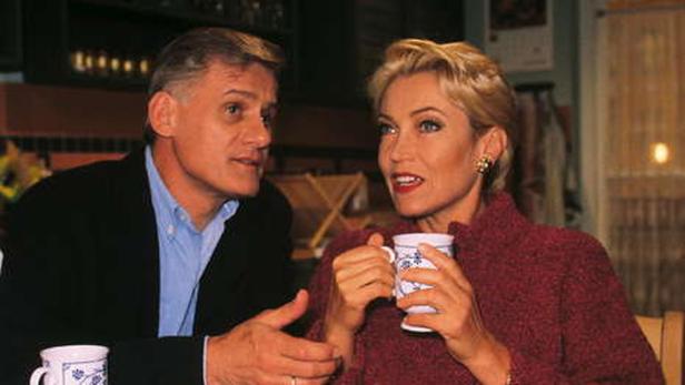 Ein Mann und eine Frau sitzen an einem Tisch, sie hält eine Tasse in der Hand.