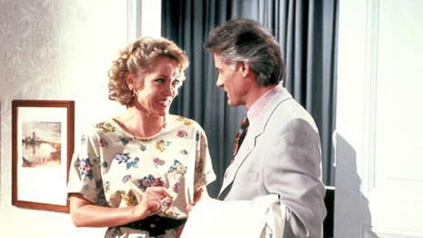 Eine Frau mit Blumenmusterbluse unterhält sich mit einem Mann im Anzug.