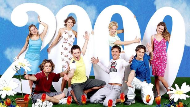 Eine Gruppe junger Leute posiert vor der Zahl 2000 auf einer Wiese mit Blumen.