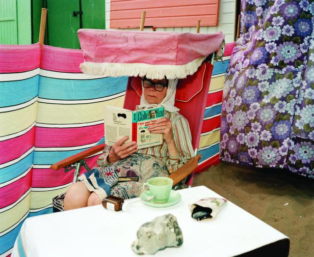 Eine ältere Frau liest am Strand das Buch „I kiss your little madame“ von Colin Reid.