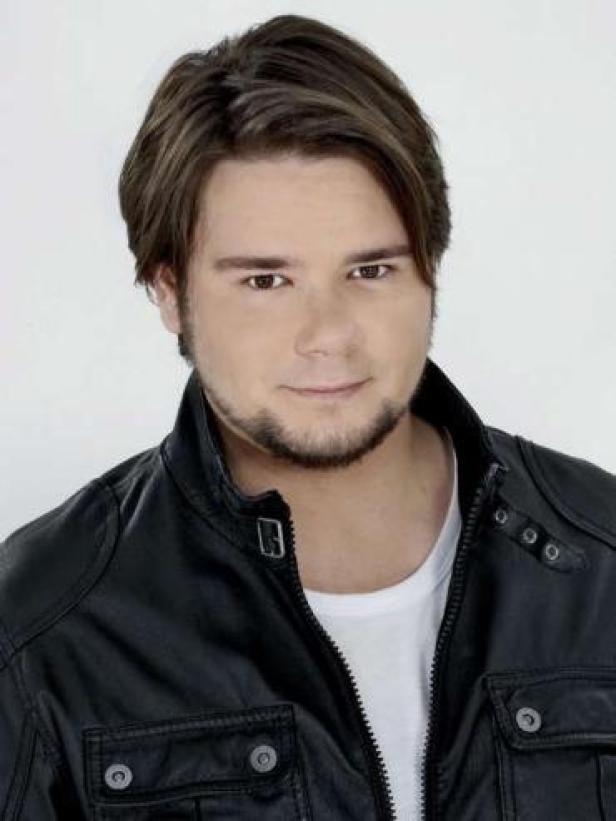 Ein Mann mit braunen Haaren und Bart trägt eine schwarze Lederjacke.