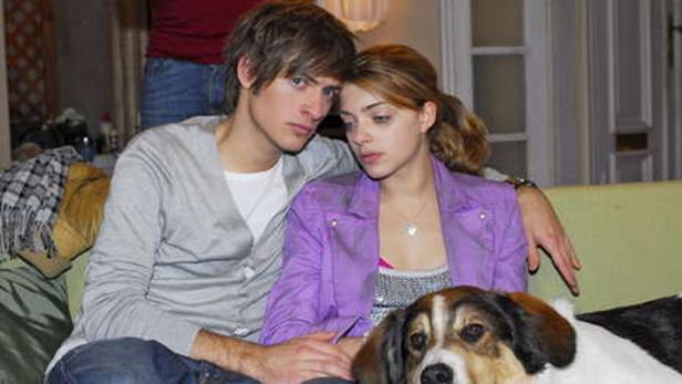 Ein junges Paar sitzt mit einem Hund auf einem Sofa.