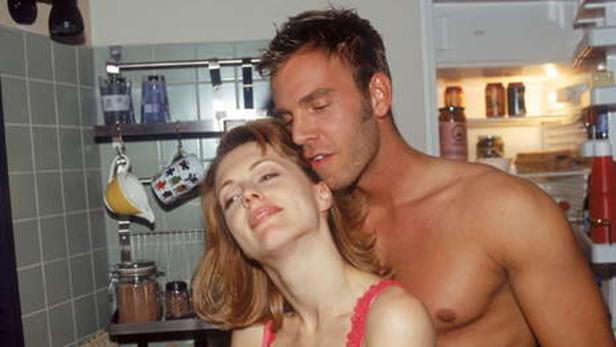 Ein Mann umarmt eine Frau in einer Küche vor einem offenen Kühlschrank.