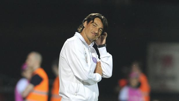 Ein Mann in Trainingskleidung lächelt und kratzt sich am Kopf.