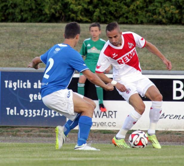 Zwei Fußballspieler kämpfen um den Ball auf einem grünen Rasen.