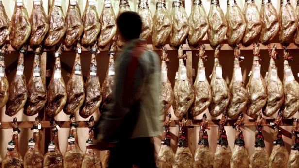 Ein Mann geht an einer Wand mit hängenden Jamón-Schinken vorbei.