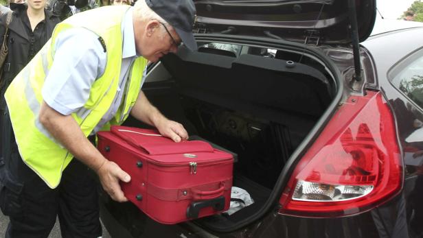 Ein Polizist in Warnweste verstaut einen roten Koffer im Kofferraum eines Autos.