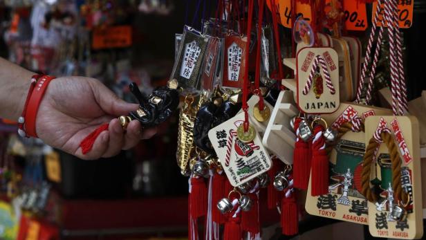 Ein Mann hält einen Glücksbringer vor einem Stand mit japanischen Souvenirs in Asakusa, Tokio.