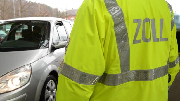 Ein Zollbeamter in gelber Jacke steht neben einem Auto.