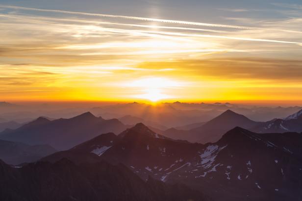Sonnenaufgang über einer Bergkette mit vereinzelten Schneeflächen.