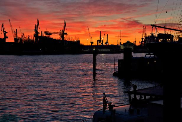 Silhouette von Kränen und Schiffen im Hamburger Hafen bei Sonnenuntergang.