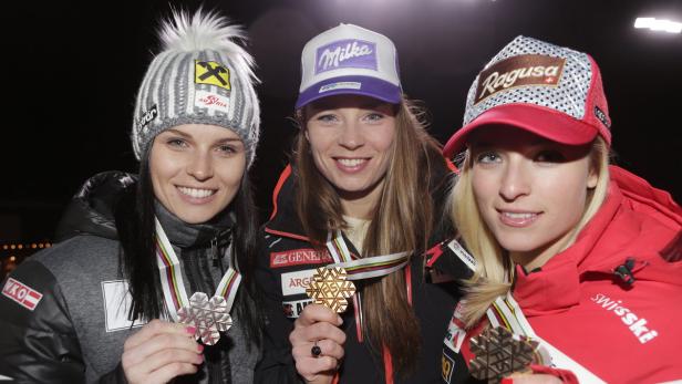 Drei Skirennläuferinnen mit Medaillen und Mützen von Sponsoren.