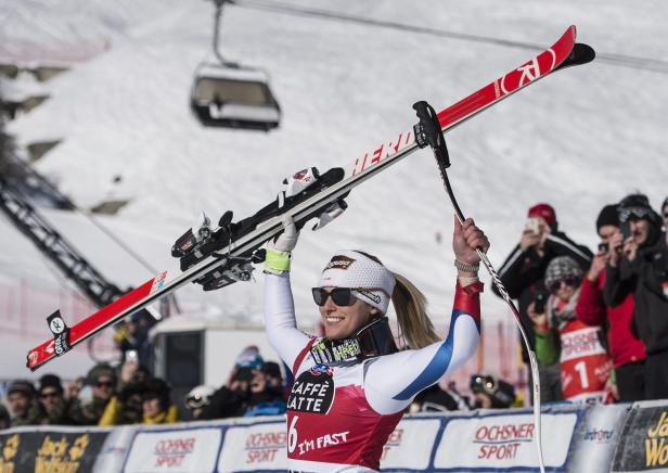 Eine Skirennläuferin jubelt mit erhobenen Skiern vor einer Zuschauermenge.