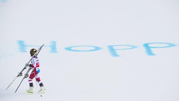 Eine Skirennläuferin trägt ihre Skier vor dem Schriftzug „Hopp“ im Schnee.