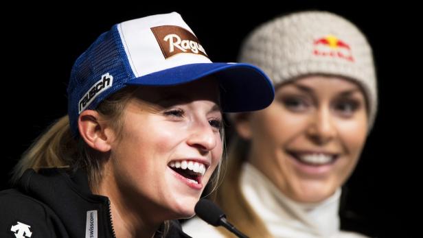 Eine lächelnde Skirennläuferin mit Kappe spricht in ein Mikrofon, eine weitere Skirennläuferin im Hintergrund.