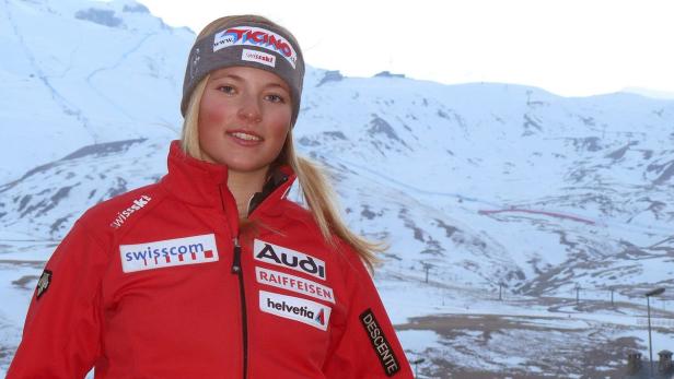 Eine Skirennläuferin in roter Jacke vor einer verschneiten Berglandschaft.