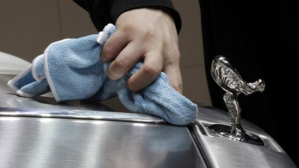Eine Hand poliert mit einem blauen Tuch die Kühlerfigur eines Rolls Royce.