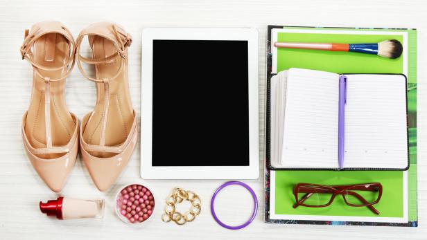 Ein Tablet, Schuhe, Make-up und Büroartikel liegen auf einem Tisch.
