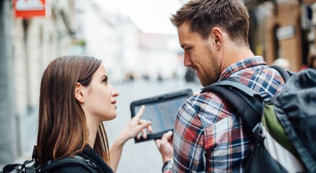 Ein Paar mit Rucksäcken betrachtet eine digitale Karte auf einem Tablet.