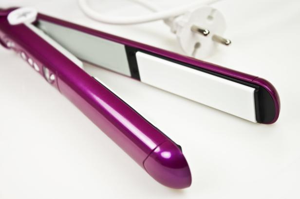 Ein geöffnetes, violettes Glätteisen liegt auf einem weißen Hintergrund.