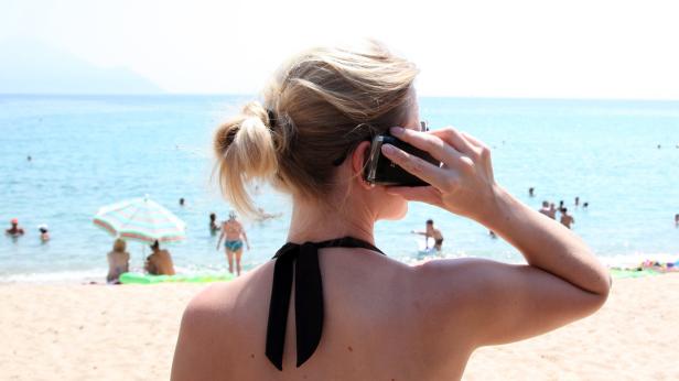 Eine Frau macht am Strand ein Foto mit ihrem Handy.