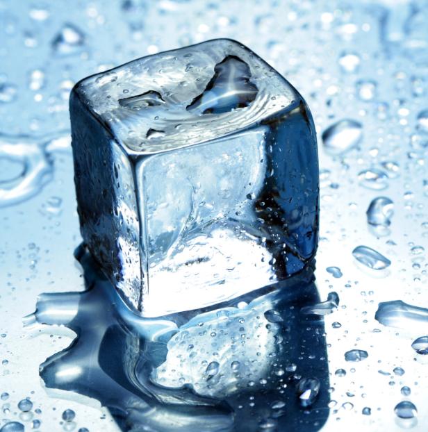 Ein einzelner Eiswürfel schmilzt auf einer glänzenden Oberfläche.