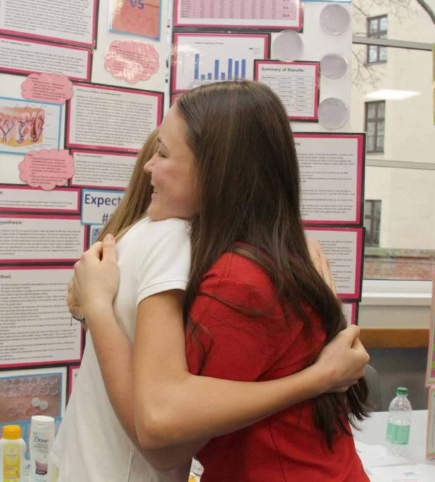 Zwei junge Frauen umarmen sich vor einer Präsentationstafel.