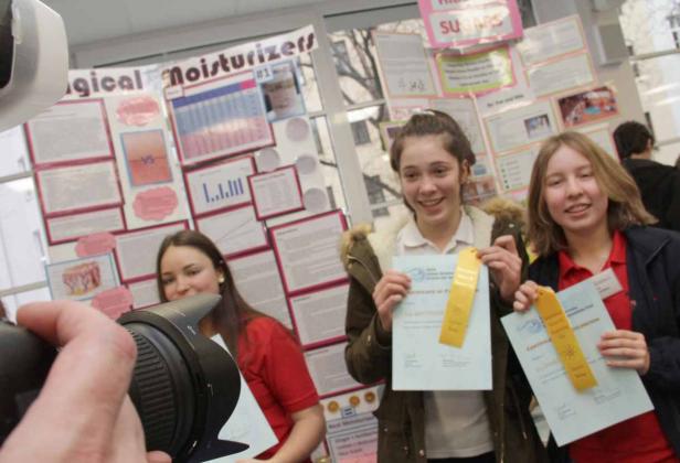 Zwei Mädchen präsentieren stolz ihre Auszeichnungen bei einem Wissenschaftswettbewerb.