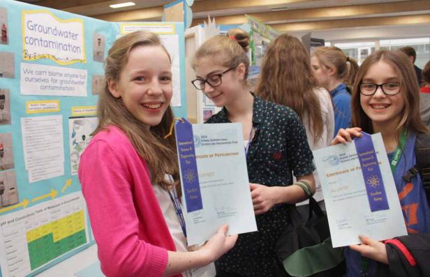 Drei Mädchen präsentieren ihre Projekte auf einer Wissenschaftsmesse und halten Urkunden in der Hand.