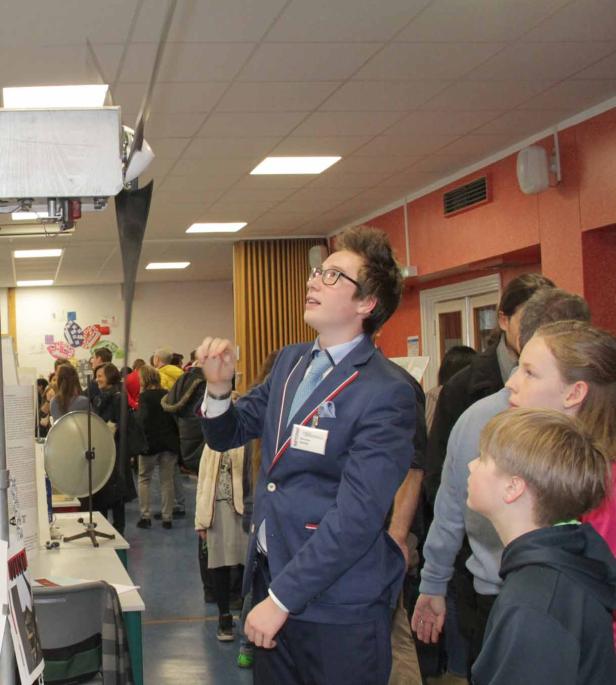 Ein junger Mann präsentiert ein technisches Projekt auf einer Bildungsmesse.