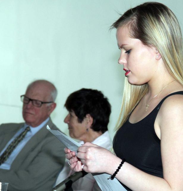 Eine junge Frau liest vor Publikum von einem Blatt Papier ab.