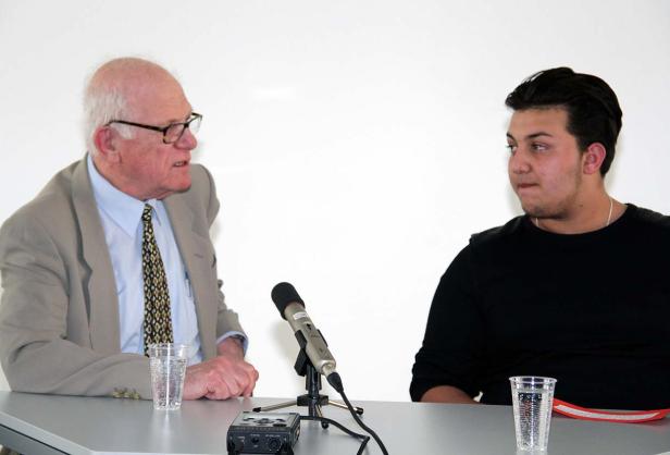 Zwei Männer sitzen an einem Tisch mit Mikrofon und diskutieren.