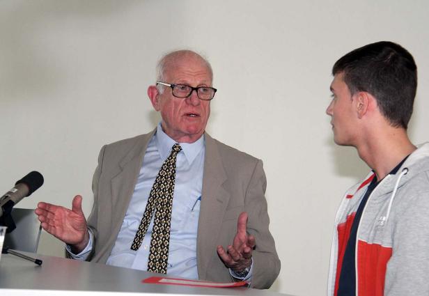 Ein älterer Mann mit Brille gestikuliert, während ein junger Mann ihm zuhört.