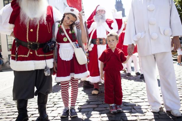 Eine Gruppe von Menschen, darunter Kinder, verkleidet als Weihnachtsmänner und Elfen, auf einer Straße.