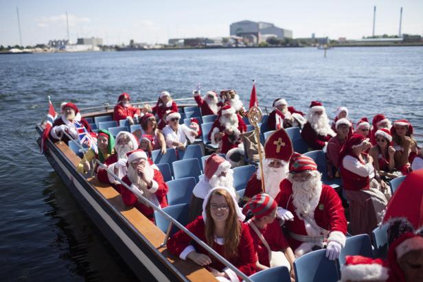 Eine Gruppe von als Weihnachtsmänner und -frauen verkleideten Menschen fährt mit einem Boot auf dem Wasser.