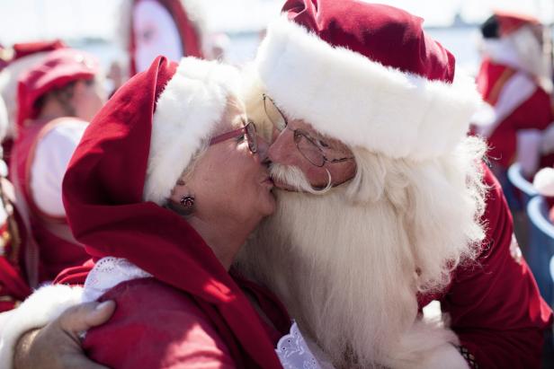 Ein Weihnachtsmann und eine Frau im Weihnachtskostüm küssen sich.