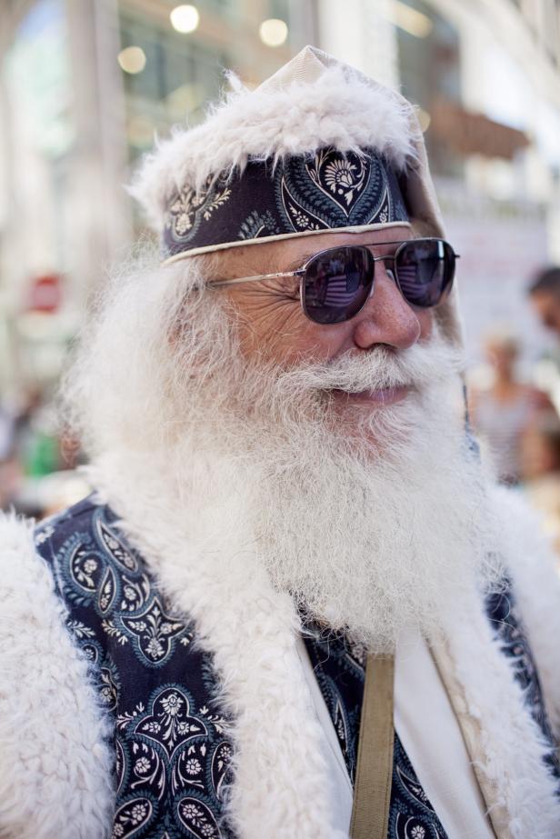 Ein älterer Mann mit langem, weißem Bart und Sonnenbrille trägt einen verzierten Hut und eine Weste.