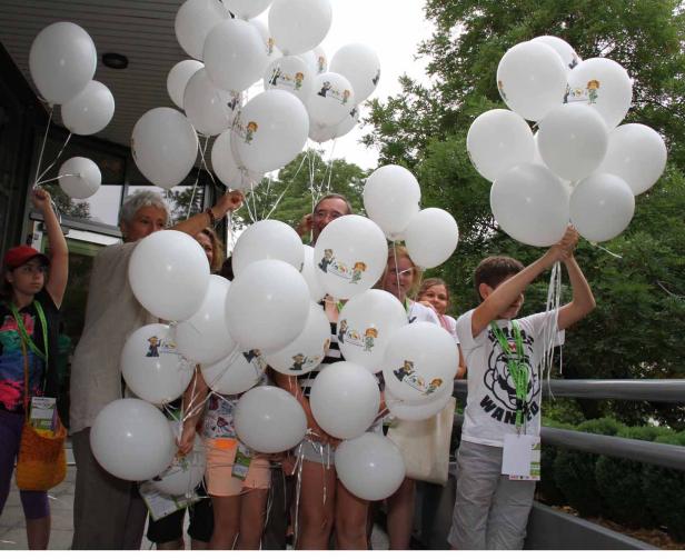 Eine Gruppe von Menschen hält weiße Luftballons mit einer Zeichnung darauf.