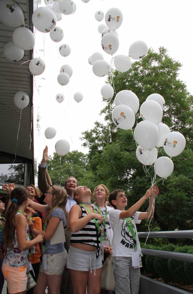 Eine Gruppe von Kindern und Erwachsenen lässt weiße Ballons mit Motiven in den Himmel steigen.